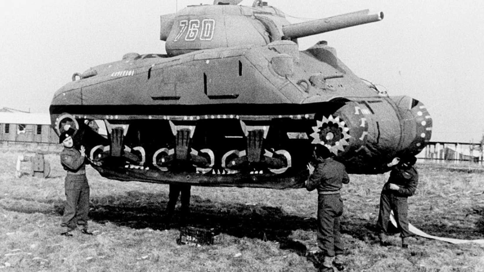 Four Ghost Army soldiers lift an inflatable Sherman tank during World War II.