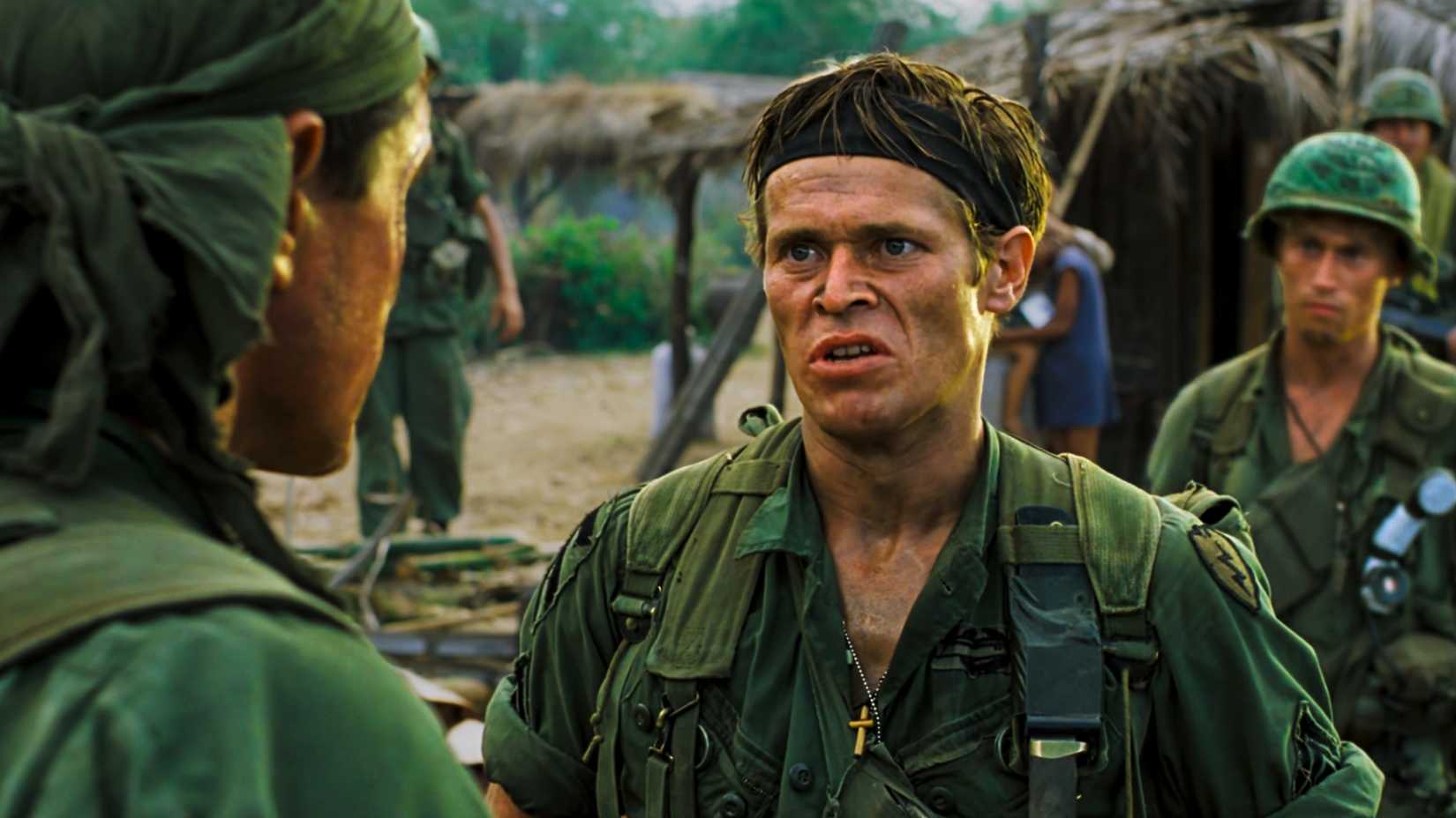 Willem Dafoe as Army Sgt. Elias Grodin wearing a combat uniform and headband while speaking to another soldier in Platoon.