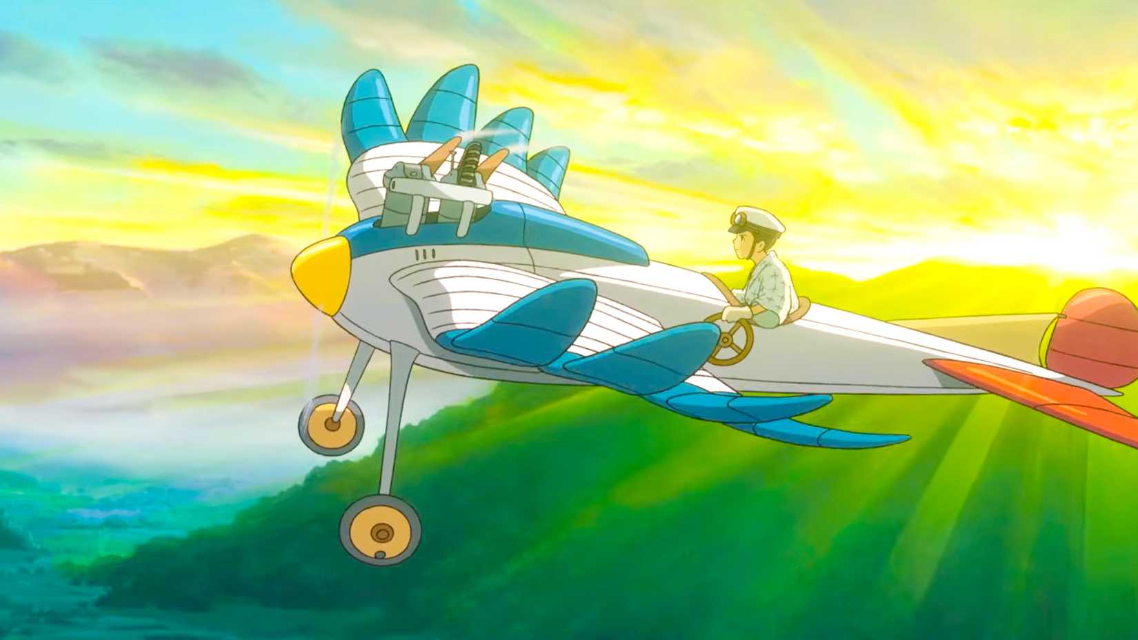 Animated aircraft designer Jiro Horikoshi rides in a colorful experimental airplane above green hills in Studio Ghibli's The Wind Rises.